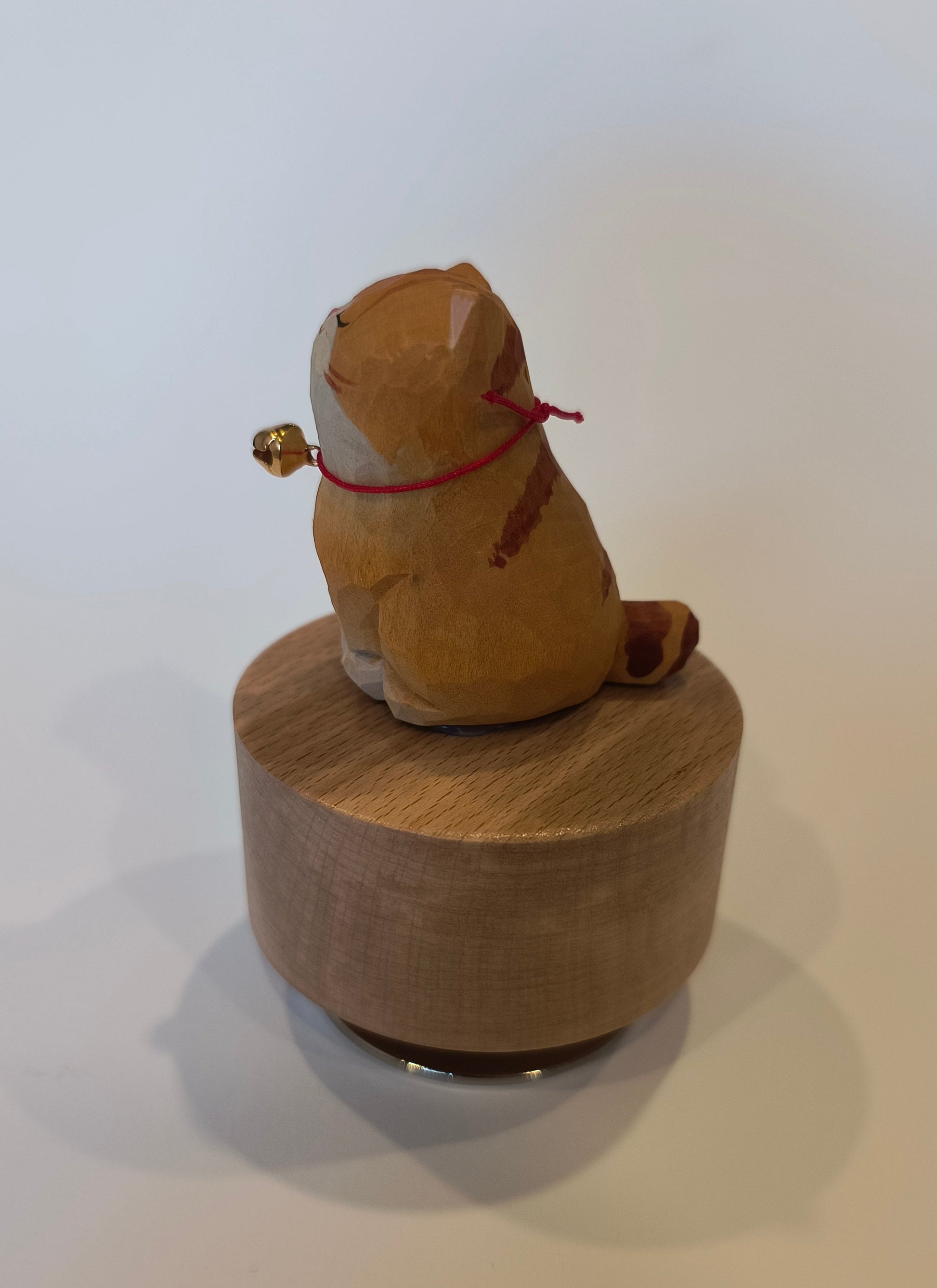 Wooden cat-shaped object with a red string and gold bell on a white background