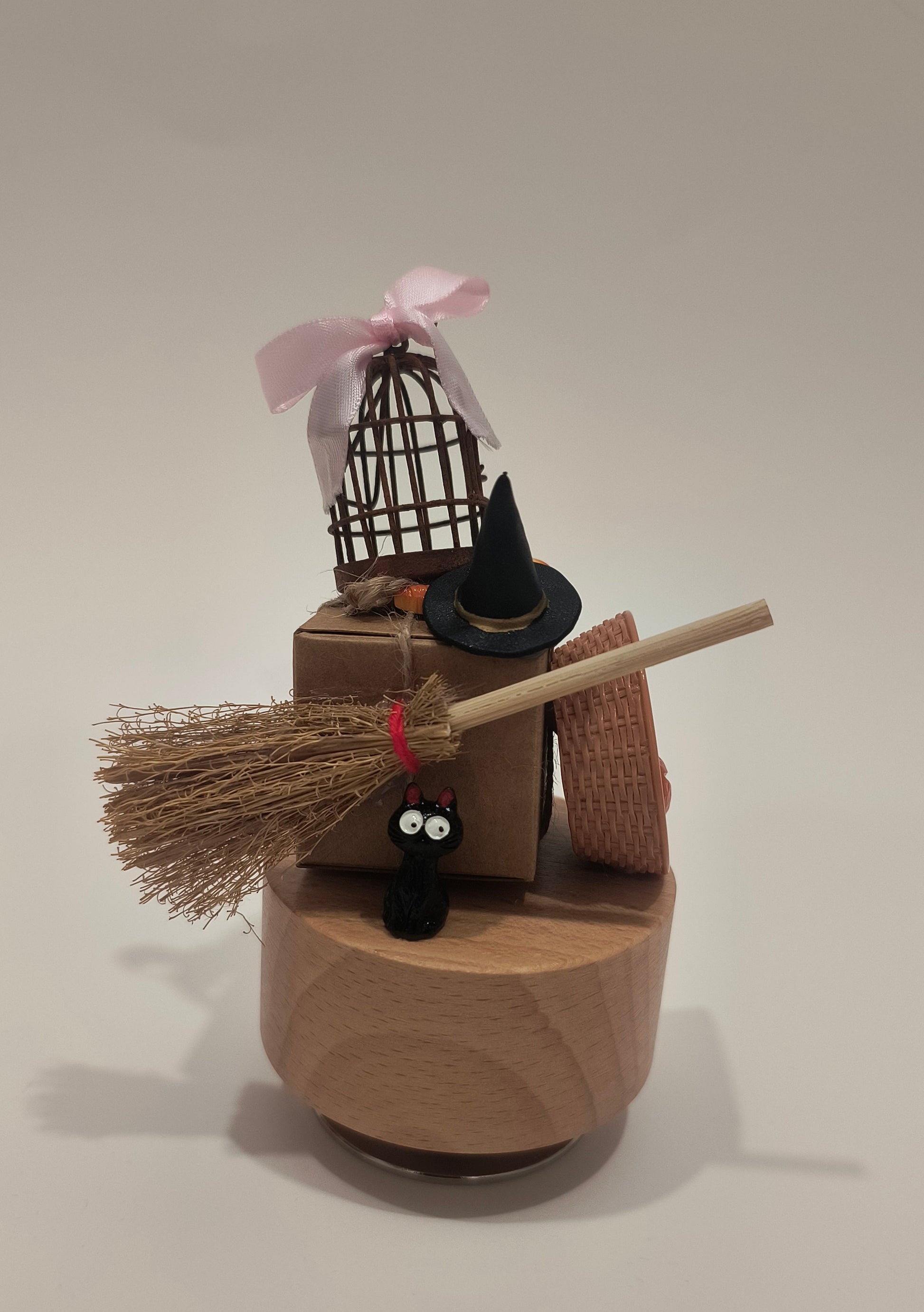 Small decorative witch's cauldron with a broom and black cat on a plain background