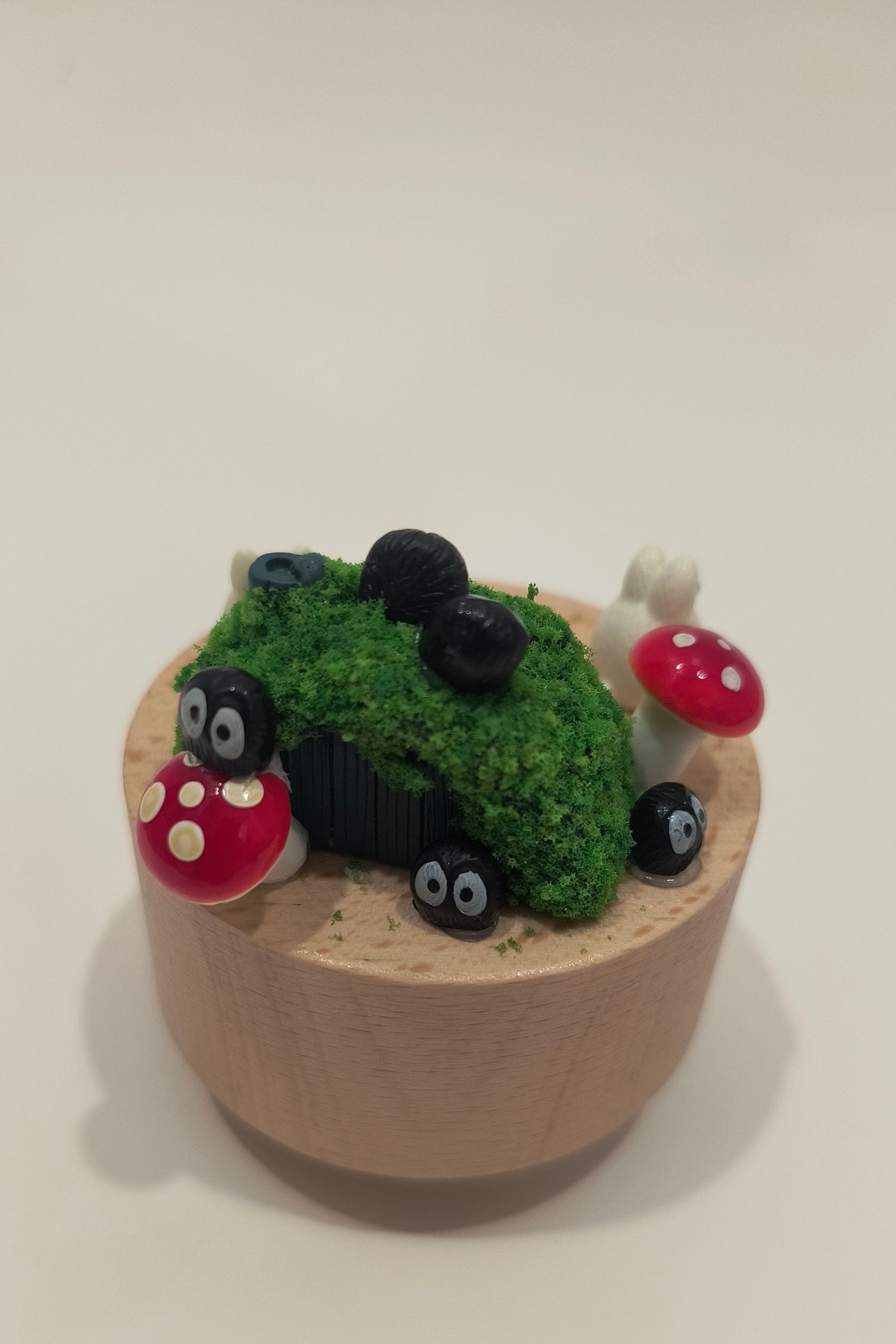 Small decorative item resembling a cup with green grass, black stones, and red mushrooms on a white background