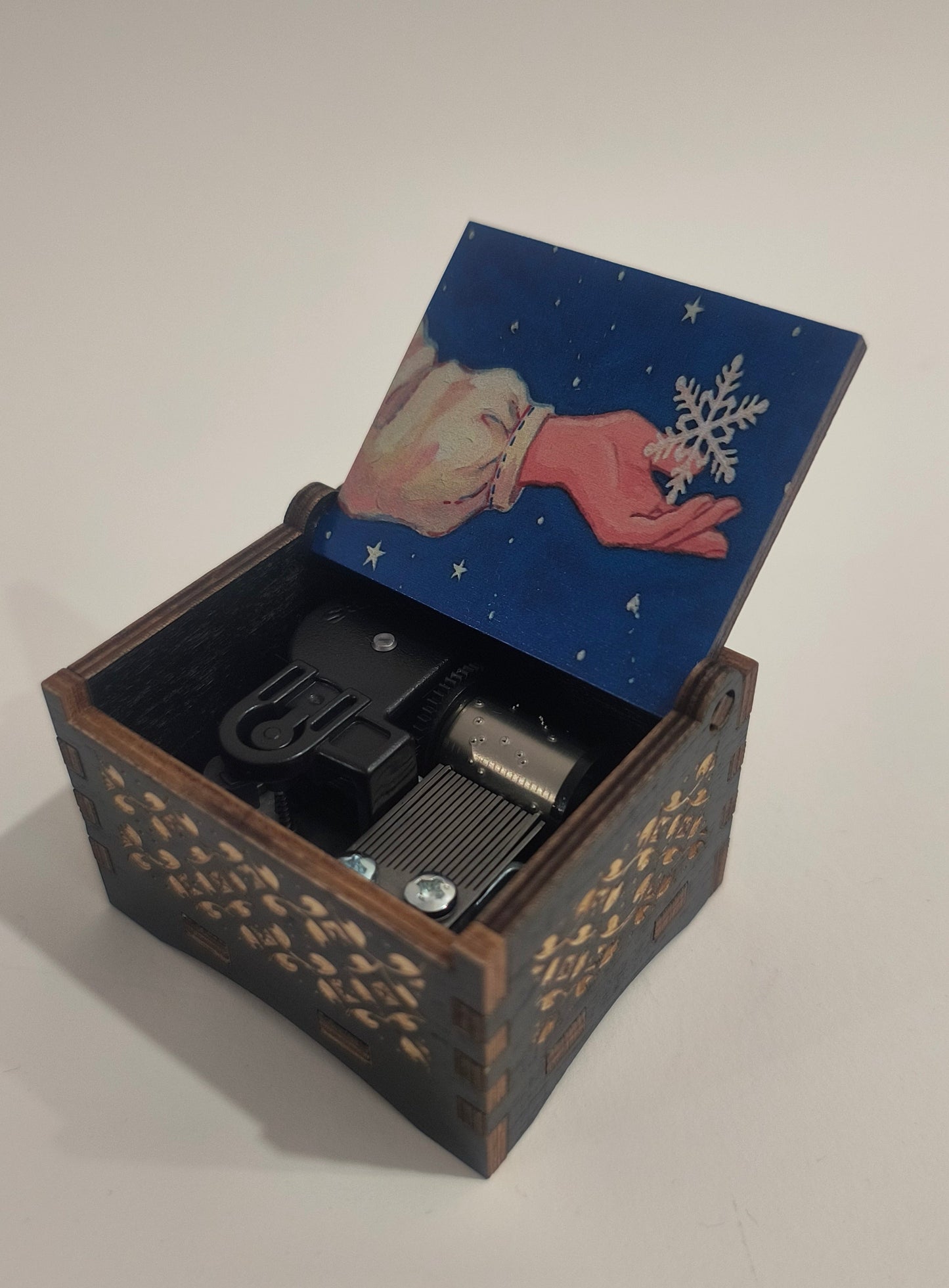Decorative box with a hand holding a snowflake design on the lid, open to reveal a black object inside.