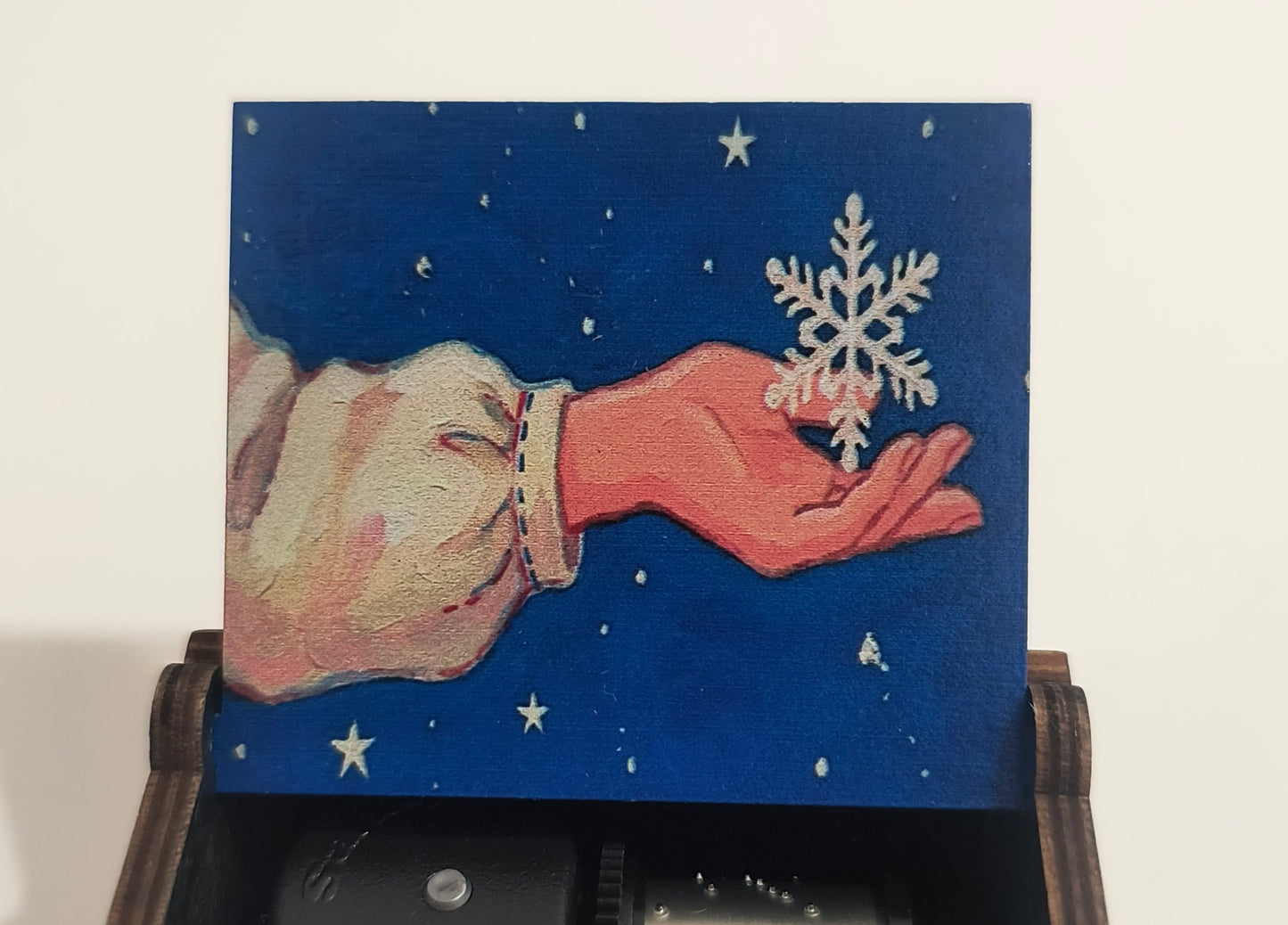 Wooden box with a hand holding a snowflake design on the lid, containing a vintage-style camera.