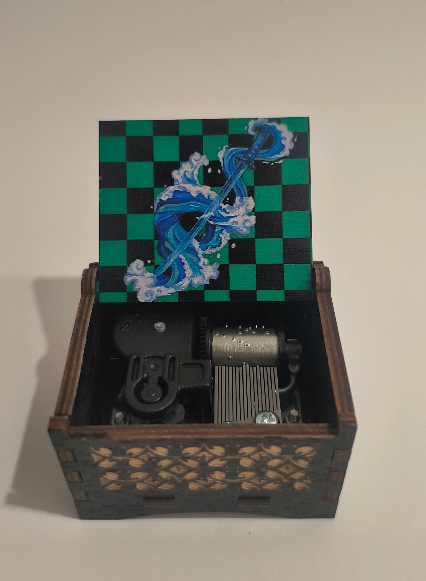 A decorative wooden wall-mounted box with one door painted green and black checkers and blue wave artwork, shown open to reveal internal mechanical components.