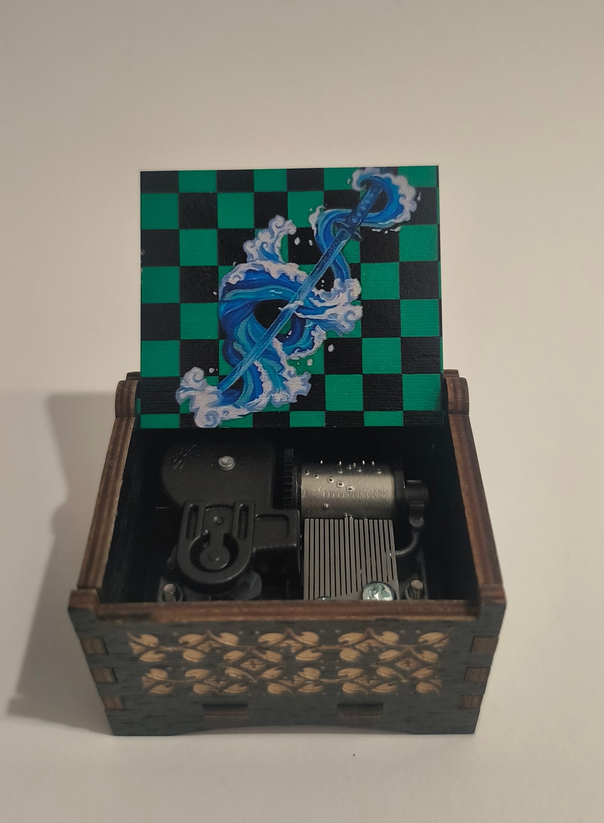 A decorative wooden wall-mounted box with one door painted green and black checkers and blue wave artwork, shown open to reveal internal mechanical components.